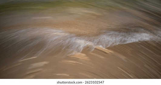 Blurred ocean waves create a dynamic abstract pattern on the sandy beach