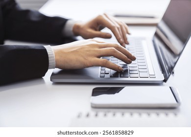 With a blurred office environment in the backdrop, the image focuses on a woman's hands typing on a state-of-the-art laptop keyboard