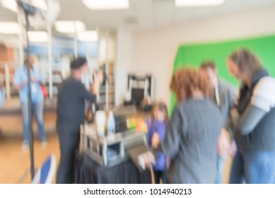 Blurred Open Space Onsite Photo Booth At Local Event In Irving, Texas, USA. Photographer With Assistant Taking Free Family Photos With Large Green Screen Backdrop. People Review Instant Print Photos