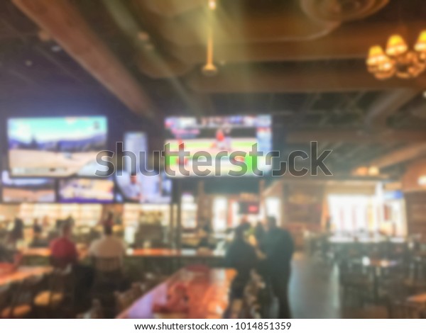 Blurred\
open space sport bar with large wall mount flat-screen TV, classic\
wooden table, chair. People drink craft beer, hanging out, resting,\
watching sport. Happy Hour and night club\
concept