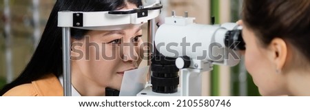 blurred ophthalmologist measuring eyesight of asian woman on vision screener, banner