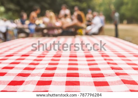 blurred party on background, fun / spring concept. Red checkered tablecloth texture top view with abstract green bokeh from garden. Abstract blur people picnic in the park.  Blurred concept.