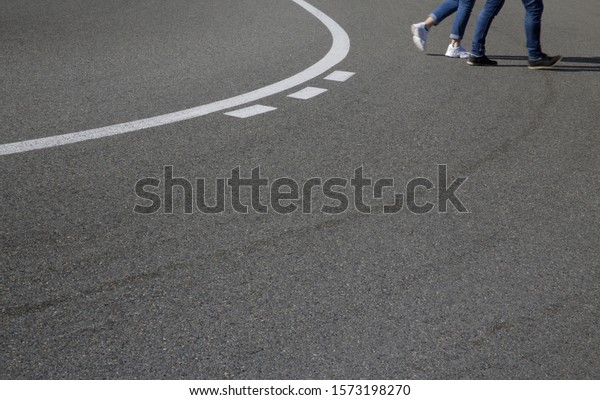 Blurred pedestrians\' feet and legs in motion on\
steep turn. Danger. Accident road crossing. Dangerous speed\
driving. Road bend with solid and broken white marking. Accidental\
road traffic or car\
race.