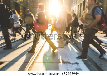 Blurred people crossing the street. Background ready image with fast moving people walking across the road in Toronto with sun flares in the middle. Travel and commuting concepts