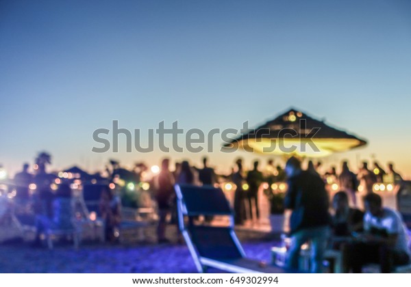 Blurred people having\
sunset beach party in summer vacation - Defocused image - Concept\
of nightlife with cocktails and music entertainment - Warm filter\
with blurry bokeh