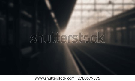 A blurred perspective of an empty railway platform with soft light emanating from the distance in a moody monochromatic urban environment