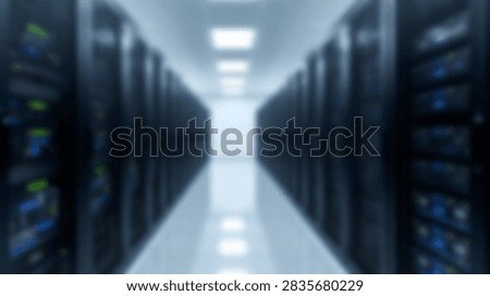 A blurred perspective view down a long corridor in a modern data center filled with server racks and illuminated by overhead lights.
