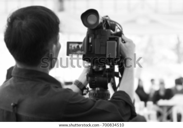 Blurred photo black and white -\
professional cameraman - covering on event with a video\
