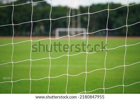 Blurred photo of football goal's net with background of firm grass pitch ground and the opposite site goal. Sport field equipment for background.