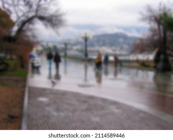 Blurred Photo. People Walk Along The Promenade Near The Sea In Cloudy Weather. 