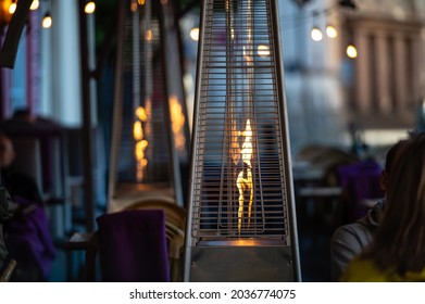blurred photo of street cafe terrace decorated with flame heate, evening street lights, fcozy mood