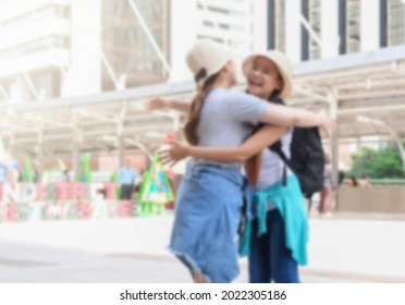 Blurred Photo Of Two Asian Female Traveler Hugging And Smile Each Other When Meets At Outdoor City Landmark Background. Light Effect.