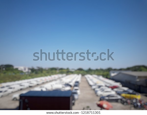 Blurred picture\
of outdoor car parking lot. There are a lot of car is parking.\
Background is blue sky at day.\
