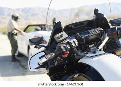 Blurred Police Officer Talking To Driver Of Stopped Car On Desert Highway With Focus On Motorbike