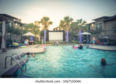 Blurred Pool Party At Apartment Complex In America. Family Oriented Event With Kids Swimming And Huge Inflatable Outdoor Projector For Open Air Cinema