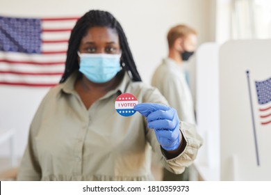 Blurred portrait of African-American woman holding I VOTED sticker while standing t polling station on post-pandemic election day, copy space