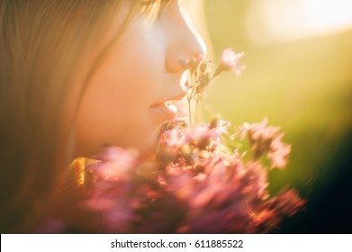 blurred portrait of the girl and wildflowers near lips on a sunset, springtime background