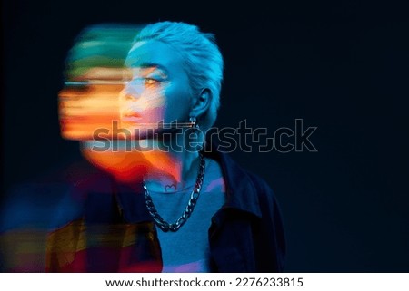 Blurred portrait of young blonde girl with neon colored face posing over dark background in blue neon lights. Concept of art, modern style, cyberpunk, futurism and creativity