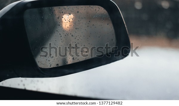 Blurred, Rain drops on a car window with the\
mirror in the bokeh background During Holiday trip Caution during\
the rainy weather. Selective focus raindrops on wing car mirror.\
autumn concept.