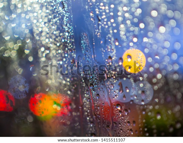 Blurred rain drops texture on car window with\
colorful bokeh abstract\
background.