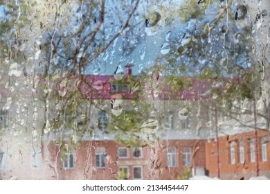 Blurred raindrops on the window pane and outlines of houses behind.