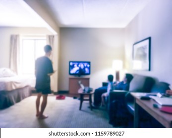 Blurred Rear View Of An Asian Family Relaxing On A Sofa And Watching TV At American Hotel
