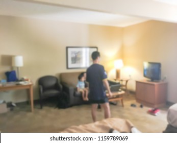 Blurred Rear View Of An Asian Family Relaxing On A Sofa And Watching TV At American Hotel