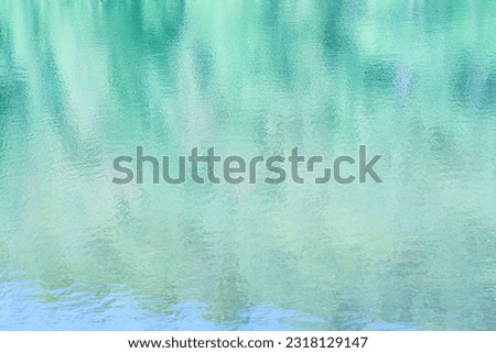 Blurred reflections of trees, forest and blue sky in lightly rippling water of a lake. Shades of blue, teal, turquoise and green.Suitable as background.