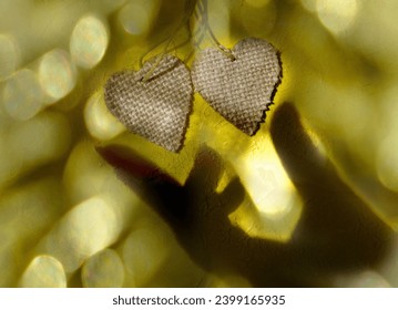 Blurred shadow of female hand and two wooden heart on rough yellow wall background. Sunlight and  crossed lines shadows, Minimal aesthetics. Abstract, play of light and shadow, shadow play illusion