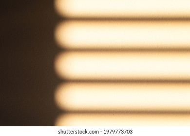 Blurred Shadow Of Natural Golden Sunset Shining Thru Window Shutter Reflect On Rough Wall. Unfocused Striped Pattern On Textured Indoor Space. Abstract Blur, Dark And Light. Concept Of Illusion.