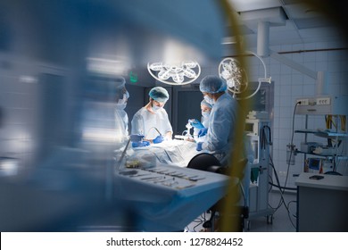 Blurred Shot Of Group Of Professional Surgeons At Work In Operating Room. Emergency Case, Surgery, Medical Technology, Health Care Cancer And Disease Treatment Concept