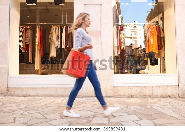 屋外の街で おしゃれな若い女性が歩く ぼやけた横の姿が 服を着た店のショッピングウィンドウを通り過ぎた 消費者の生活 観光客の訪問と支出 紙袋の持ち運び の写真素材 今すぐ編集