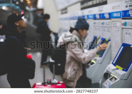 Blurred side view of passengers using ticket vending machines to purchase train tickets at a railway station in Osaka, Japan.
