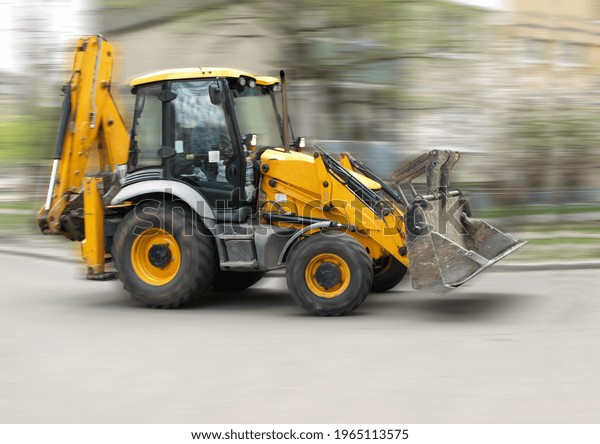 Blurred silhouette of a front loader excavator\
moving between houses
