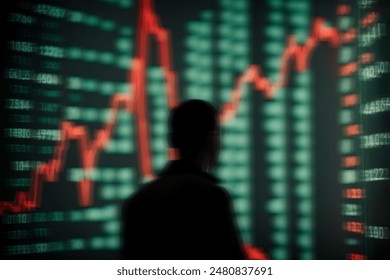 A blurred silhouette of a person is seen in the foreground with a background of a stock market chart displaying a fluctuating trend line in red and green. - Powered by Shutterstock