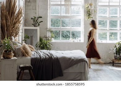 Blurred Silhouette Of Young Adult Woman Walking At Comfortable Bedroom With Interior Design In Boho Chic Style. Lady In Dress Standing Near Cozy Bed, Enjoying Morning At Home