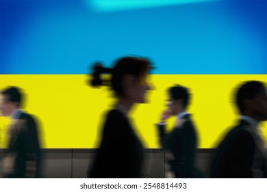 Blurred silhouettes of diverse business people walking against a vibrant Ukraine flag, conveying motion and diversity in a corporate setting. Business people walking in front of Ukraine flag. - Powered by Shutterstock