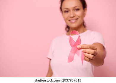 Blurred smiling mixed race woman in pink t-shirt hold satin ribbon in her hand. Breast and abdominal cancer awareness, October Pink day on colored background, copy space. Breast cancer support concept