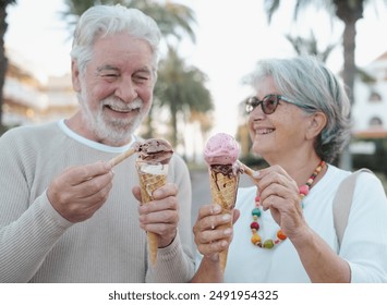 Blurred smiling retired couple having fun eating a fresh ice cream cone in the park. Focus on the two ice creams that are melting. Joyful senior lifestyle concept. - Powered by Shutterstock