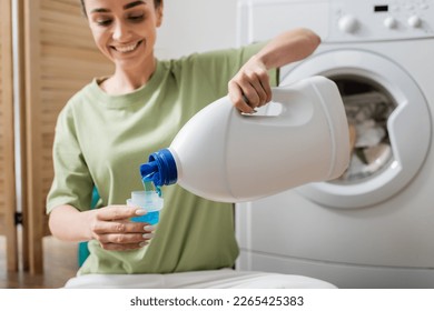 Blurred smiling woman pouring washing liquid in cap near machine in laundry room - Powered by Shutterstock