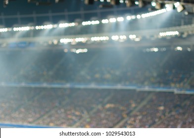 Blurred soccer stadium or ather sport arena at night with projector and stands full of people, fans, crowd - Powered by Shutterstock