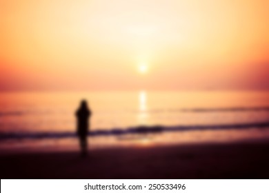 Blurred And Soft Focus, Silhouette Of Woman Alone And Wave On The Beach With Sunset In The Sea