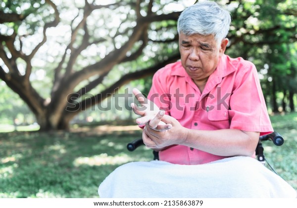 Blurred\
soft images of Asian elderly man, Patients wrist pain hands, due to\
a nervous system illness and paralysis, On blur tree in garden \
background, to elderly and health care\
concept.