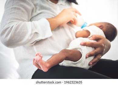 Blurred Soft Images Of Mother Sitting On Bed, And Feed Milk From Bottle Milk To Her 12-day-old African Baby Black Skin Newborn Son, This Picture Focused On Foot Baby, To Family And Food Infant Concept