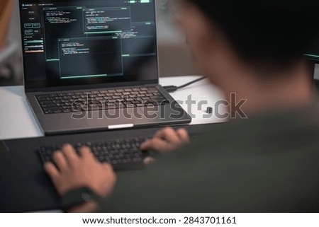 Blurred software developer writing code on a laptop in a dark workspace focused on artificial intelligence programming and advanced technology development