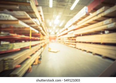 Blurred Stack New Wooden Bar On Shelves Inside Lumber Yard Of Large Hardware Store In America. Rack Of Fresh Mill/cut Wood Timber With Flatbed Cart, Manual Forklift In Warehouse. Industrial Background