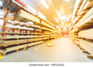 Blurred Stack New Wooden Bar On Shelves Inside Lumber Yard Of Large Hardware Store In America. Rack Of Fresh Mill/cut Wood Timber With Flatbed Cart, Manual Forklift In Warehouse. Industrial Background