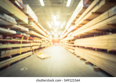 Blurred Stack New Wooden Bar On Shelves Inside Lumber Yard Of Large Hardware Store In America. Rack Of Fresh Mill/cut Wood Timber With Flatbed Cart, Manual Forklift In Warehouse. Industrial Background