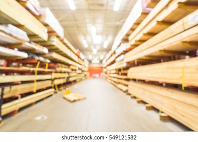 Blurred Stack New Wooden Bar On Shelves Inside Lumber Yard Of Large Hardware Store In America. Rack Of Fresh Mill/cut Wood Timber With Flatbed Cart, Manual Forklift In Warehouse. Industrial Background