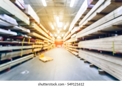 Blurred Stack New Wooden Bar On Shelves Inside Lumber Yard Of Large Hardware Store In America. Rack Of Fresh Mill/cut Wood Timber With Flatbed Cart, Manual Forklift In Warehouse. Industrial Background